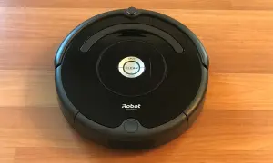 Un robot aspirador Roomba, uno de los modelos antiguos, descansa sobre un suelo de madera.