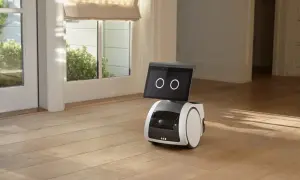 El robot Alexa Astro, con pantalla y ruedas, se encuentra en un suelo de madera, cerca de una puerta acristalada.