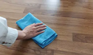 Mano con paño azul limpiando suelo laminado, ideal para saber como limpiar suelo laminado después de obra y dejarlo impecable.