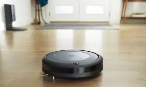 Un Roomba i3 negro aspira el suelo de madera.