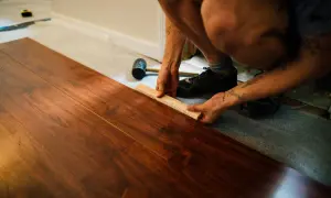 Instalando tarima flotante sobre parquet. Se muestra cómo colocar una pieza de madera con un bloque y mazo. El precio de poner tarima encima de parquet es una inversión que renueva el hogar.