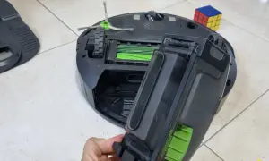Mano retirando el depósito de suciedad de un Roomba, quizás para solucionar un error 11. Un cubo de Rubik descansa cerca.