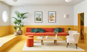 Salón moderno con sofá naranja, butacas blancas y **suelos de linóleo** amarillo vibrante. Plantas verdes y cuadros decoran el espacio.