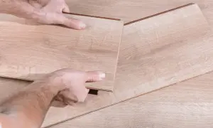 Manos desmontando una tabla de suelo laminado.