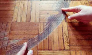 Manos señalan un arañazo profundo en un suelo de parquet de madera. Descubre cómo quitar arañazos del parquet y restaurar su brillo.
