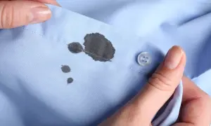 Manos sostienen una camisa azul con manchas de tinta. Aprende como quitar las manchas de tinta de la ropa.
