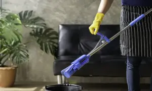 Persona con guantes amarillos y delantal a rayas friega el suelo con una mopa azul.