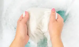 Manos lavando ropa blanca en agua con burbujas. Un chorro de agua cae sobre la tela, ayudando a como blanquear ropa blanca.