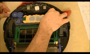 Mano arreglando un Roomba con **error 15**. Se ve la batería amarilla y las escobillas.
