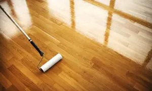 Rodillo aplicando barniz a un suelo de madera. El mantenimiento del parquet es esencial para su brillo y durabilidad.
