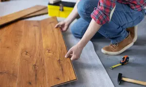 Persona instala parquet flotante de madera, colocando una tabla sobre otra.