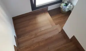 Escaleras con suelo laminado de madera, con un cesto de flores junto a una ventana.