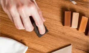 Mano lijando para reparar suelo laminado. Cera de colores y espátula listas para el retoque.