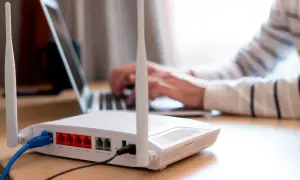 Persona frustrada intenta conectar un portátil a un router que no se enciende. Cables azules y negros conectados.