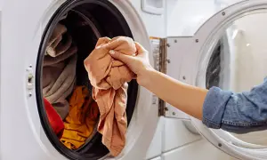 Mano saca ropa de lavadora. Un truco para limpiar lavadora con vinagre es añadirlo al ciclo de lavado.