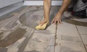 Man limpiando un suelo de baldosas con una esponja amarilla. Se ve el proceso de con que se friega el suelo.