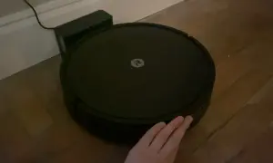 Robot aspirador Roomba con logo, conectado a su base. Una mano intenta interactuar, pero parece que hay un error 47.