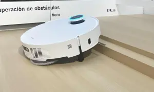 Robot aspirador blanco sobre suelo laminado, superando un pequeño desnivel.