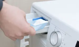 Mano agrega detergente en polvo a la lavadora.