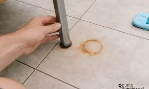 Mano levantando pata de mueble para mostrar cómo quitar manchas de óxido en el suelo de baldosas.