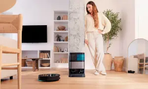 Una mujer sonríe junto a su nueva conga, un robot aspirador que limpia el suelo mientras ella descansa.