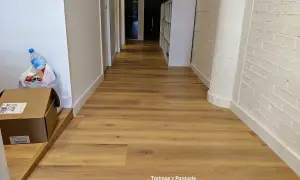 Pasillo con tarima de madera, ideal para saber como colocar tarima en pasillos. Se ven cajas y una botella de agua.