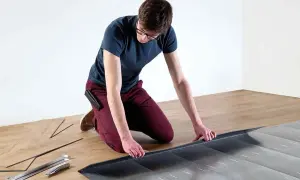 Hombre con gafas instalando suelo laminado sin experiencia. Herramientas y lamas de madera a su lado.