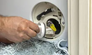 Mano retirando filtro sucio de lavadora que pierde agua por debajo. Se ve pelusa y un objeto amarillo.