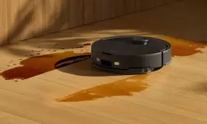 Robot aspirador negro limpiando un derrame de líquido marrón en un suelo de madera. ¿Cuánto dura un robot aspirador?