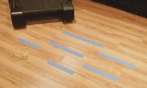 Cinta azul marca zonas de posible humedad debajo de la tarima. Un mueble oscuro está en la parte superior.