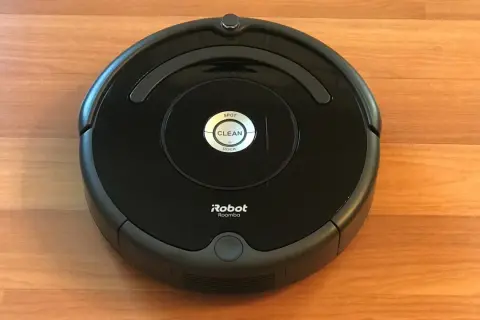 Un robot aspirador Roomba, uno de los modelos antiguos, descansa sobre un suelo de madera.