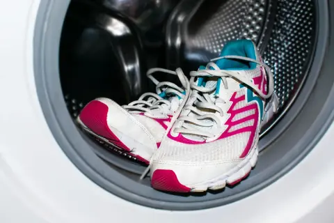 Un par de deportivas blancas con detalles fucsia y turquesa listas para lavar en lavadora.