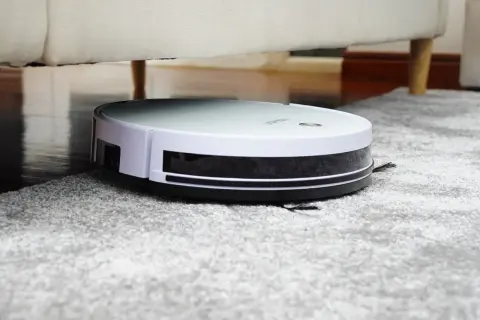 Robot aspirador Rowenta en alfombra gris, bajo un sofá. Las opiniones sobre este robot son muy positivas.