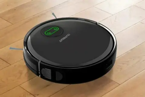 Robot aspirador negro sobre suelo de madera, listo para su reparación.