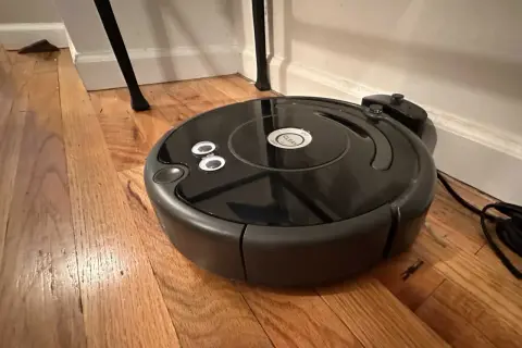 Robot aspirador negro sobre suelo de madera, parece que el roomba no detecta la base de carga.