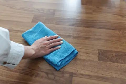 Mano con paño azul limpiando suelo laminado, ideal para saber como limpiar suelo laminado después de obra y dejarlo impecable.