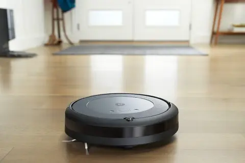Un Roomba i3 negro aspira el suelo de madera.