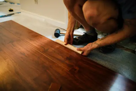 Instalando tarima flotante sobre parquet. Se muestra cómo colocar una pieza de madera con un bloque y mazo. El precio de poner tarima encima de parquet es una inversión que renueva el hogar.