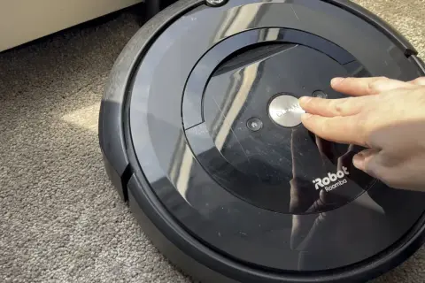 Mano presionando el botón "CLEAN" en un Roomba e5, quizás por **roomba e5 problemas**.