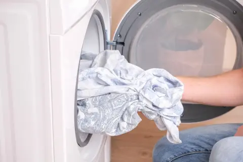 Mano saca ropa húmeda de la secadora. Parece que la secadora no seca bien, ¡qué frustración!