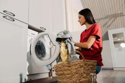Mujer con ropa sucia junto a la lavadora, lista para poner la lavadora.