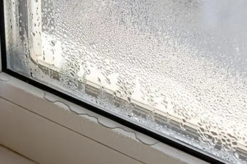 Gotas de agua cubren un cristal de ventana, mostrando cómo evitar condensación en ventanas. El agua se acumula en el alféizar.