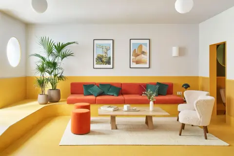 Salón moderno con sofá naranja, butacas blancas y **suelos de linóleo** amarillo vibrante. Plantas verdes y cuadros decoran el espacio.