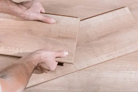 Manos desmontando una tabla de suelo laminado.