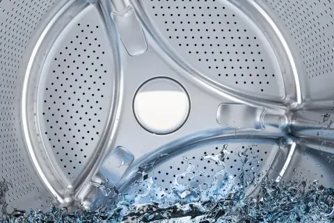 Interior de lavadora con agua salpicando. Averigua cuántos litros gasta una lavadora para optimizar tu consumo.