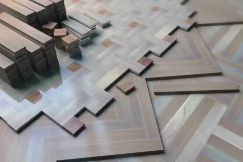 Tablas de parquet de madera apiladas y en proceso de instalación, formando un patrón de espiga. ¿Cuántas veces se puede acuchillar el parquet antes de que se desgaste?