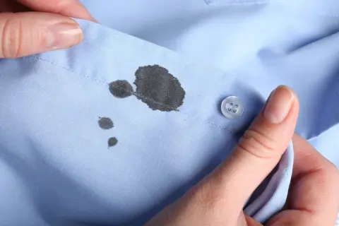 Manos sostienen una camisa azul con manchas de tinta. Aprende como quitar las manchas de tinta de la ropa.