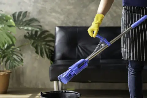 Persona con guantes amarillos y delantal a rayas friega el suelo con una mopa azul.