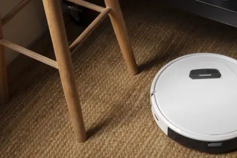 Robot aspirador Cecotec en alfombra de yute, cerca de las patas de una silla de madera. ¿Posibles averías?