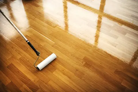 Rodillo aplicando barniz a un suelo de madera. El mantenimiento del parquet es esencial para su brillo y durabilidad.
